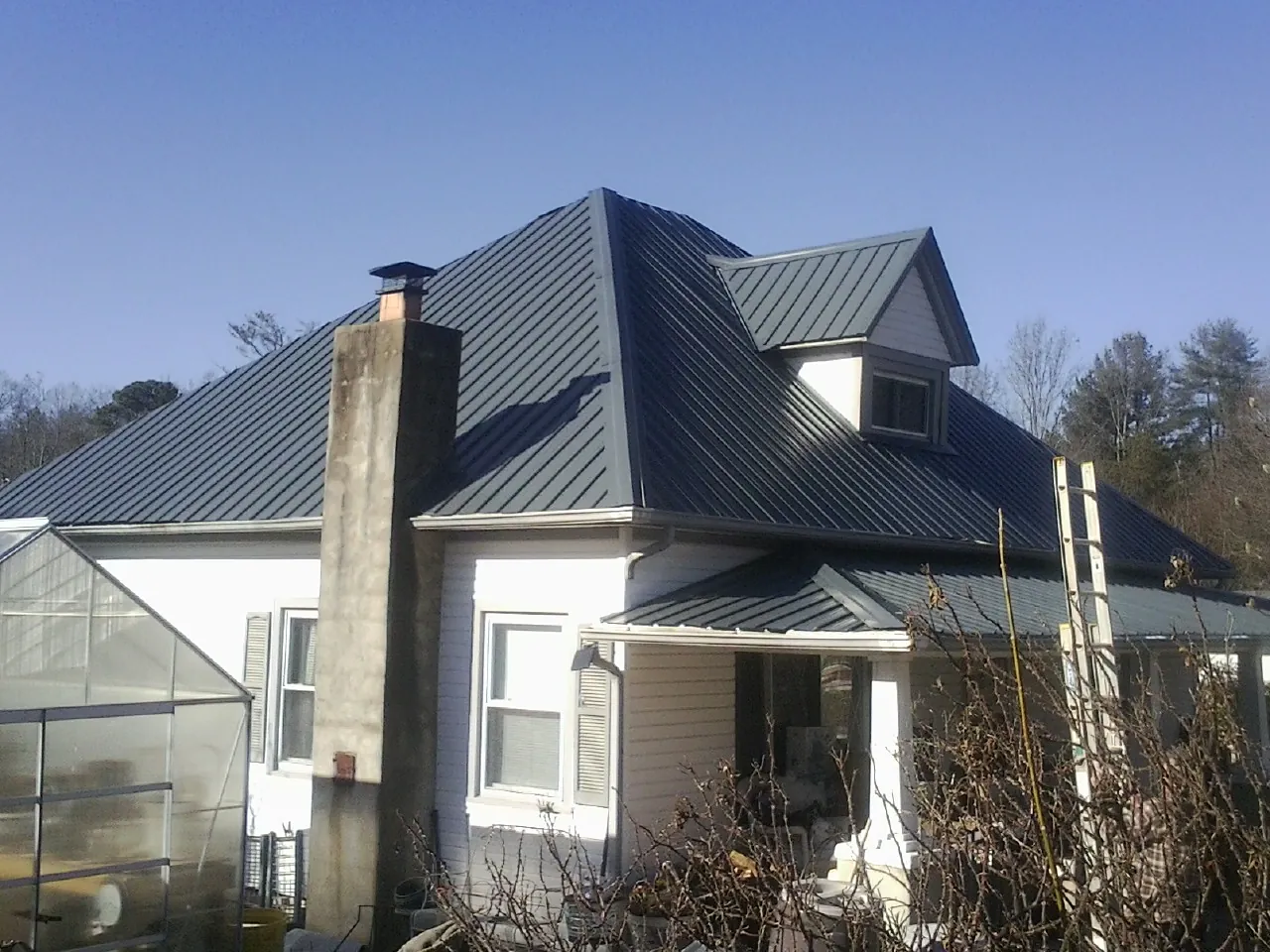 Dark blue standing seam metal roof on a white farmhouse with dormer — Slate & Tile Roof Repair by Roofing Brothers in Patricksburg