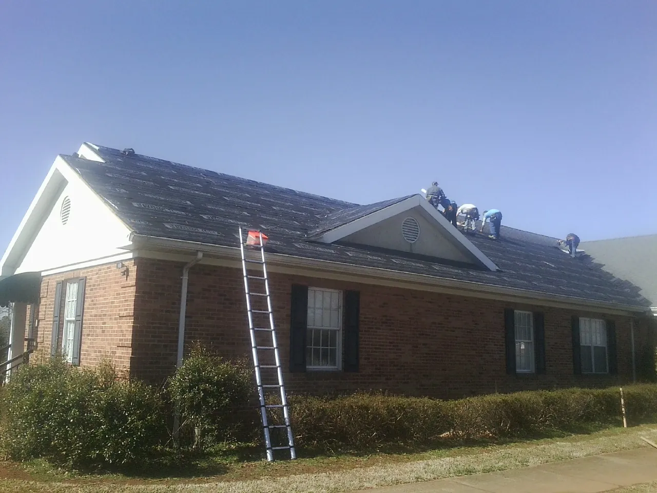 Crew tearing shingles off a brick ranch roof with a ladder set — Emergency Roof Repair work by our crew in Patricksburg