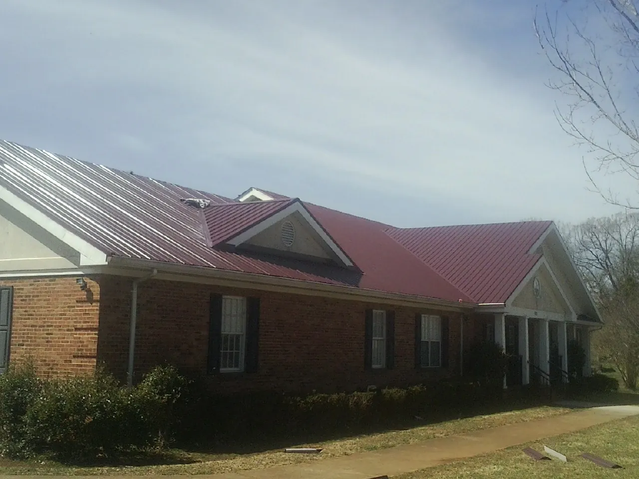 Red metal roof with gabled entries on a long brick building, from a Hail Damage Roof Repair job in Patricksburg