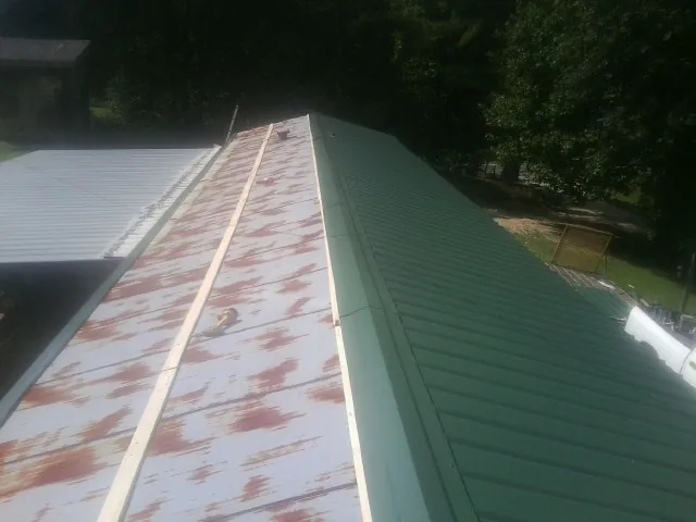 Old rusted panels beside newly installed green metal roofing — Wind Damage Roof Repair by Roofing Brothers in Patricksburg