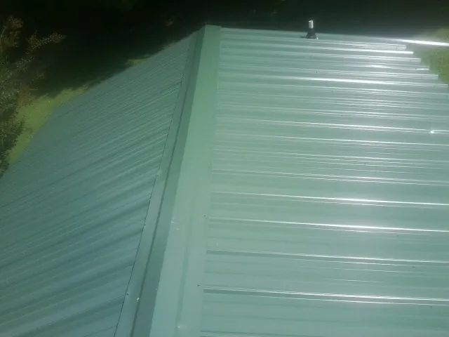 New green metal panels meeting at the ridge of a roof — Flat Roof Repair work by our crew in Patricksburg