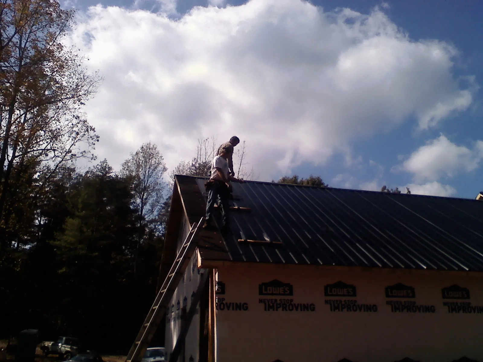 Roofer fastening dark metal panels high against a cloudy sky, from a Roof Inspection job in Patricksburg