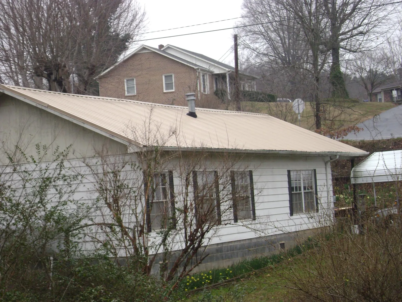 Tan metal roof on a white sided house set into a hillside — Commercial Roofing by Roofing Brothers in Patricksburg